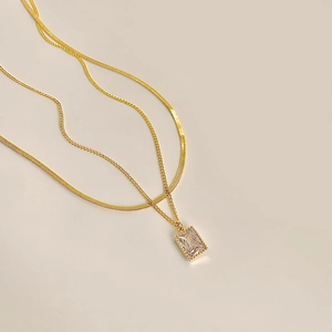 Detail view of double-layered gold necklace with flat snake chain and zircon pendant