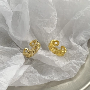 Golden woven chain open ring with Greek meander patterns on a textured background