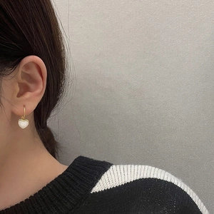 Elegant gold plated heart drop earrings with white enamel inlay worn by a model