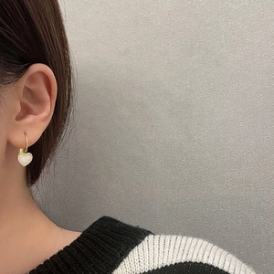 Minimalist gold hoop earrings with white heart pendant worn on model's ear