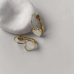 Macro detail of gold heart earrings with white pearlescent inlay on a stone prop