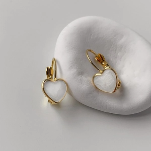Detailed 45-degree angle of heart-shaped gold-plated hoop earrings with pearl white enamel