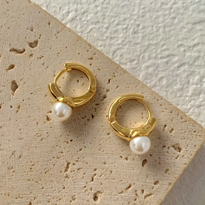 Dettaglio di orecchini a cerchio dorati con perle barocche su sfondo di pietra