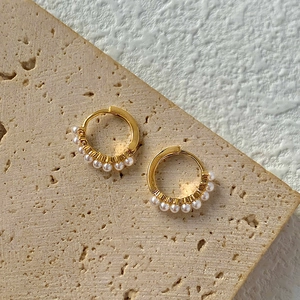 Dettaglio macro di orecchini a cerchio dorati con piccole perle barocche bianche lucide
