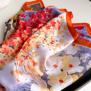 Close-up of vibrant floral printed silk scarves with orange borders and smooth texture