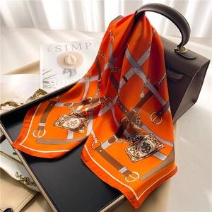 Elegant orange silk square scarf with chain pattern draped over a luxury handbag