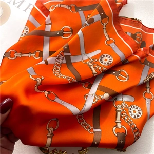 Macro view of silky orange square scarf with classic belt and chain print patterns