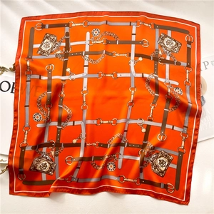 Flat lay of an orange silk scarf with chain pattern and luxury fashion magazines