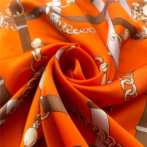 Detail of silk satin scarf with equestrian patterns showing glossy orange fabric texture