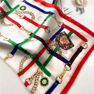 Detailed flat lay of silk scarf featuring gold chain and luxury belt patterns on white silk