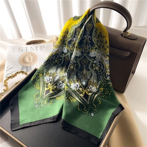 Ethnic paisley print silk scarf in yellow and green gradient draped on a leather bag