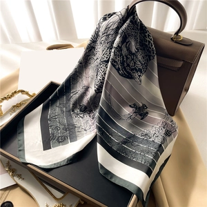 Elegant silk scarf with leopard and tropical leaf patterns draped on a brown handbag