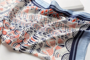 Close-up of geometric silk scarf with navy and orange abstract patterns on beige fabric