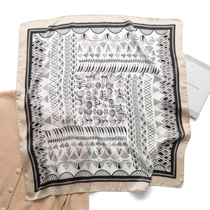 Detailed view of square silk scarf with geometric patterns laid on a beige sweater