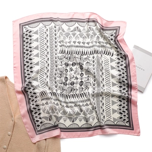 Close-up of elegant silk square scarf with geometric patterns and pink border on a white desk