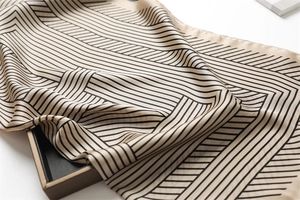 Close-up of beige silk scarf with black geometric stripes on a stylish black display tray