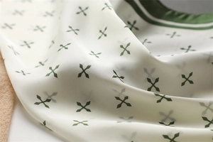 Vue détaillée du tissu soyeux avec des motifs de losanges vert foncé et des bords contrastés
