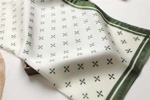 Détail du foulard carré en satin de soie avec motifs géométriques verts et bordure rayée