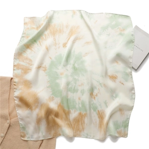 Détail à plat d'un foulard carré en soie avec motifs tie-dye vert et jaune gingembre