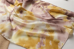 Gros plan d'un foulard en soie tie-dye montrant la texture lisse et les tons jaune rose