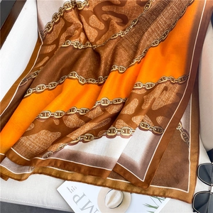Dettaglio di un foulard in seta con motivi a catena dorata e accenti arancioni