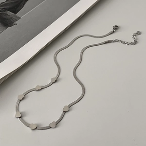 Detailed view of silver heart charms on a flat herringbone chain over white surface