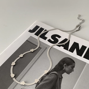 Detail of silver snake chain necklace with small polished heart pendants on a magazine