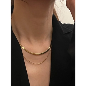 Detail of layered gold snake chain necklace featuring a flat and round polished link design