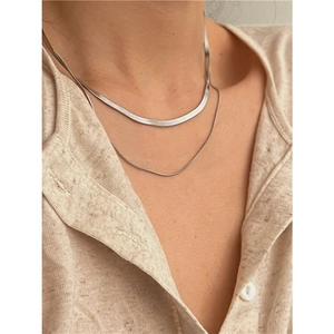 Macro detail of layered silver snake chain and fine link necklace on collarbone