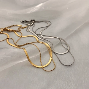 Minimalist double-layered gold and silver snake bone chain necklaces on white fabric