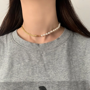Détail du collier moitié perles et moitié chaîne torsadée dorée sur le décolleté