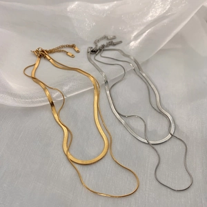 Detail of layered gold and silver snake chain necklaces with lobster clasp on white fabric