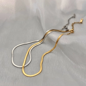 Detailed macro of gold and silver flat snake chains with lobster clasp on white fabric