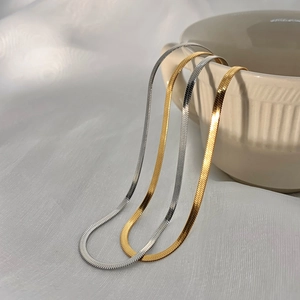 Three minimalist flat snake bone choker necklaces in gold and silver on a ceramic cup