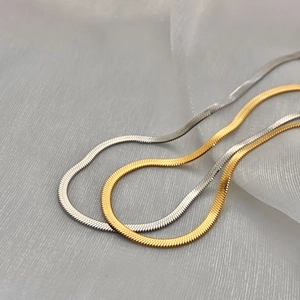 Close-up of gold and silver flat snake chain necklaces on textured soft fabric