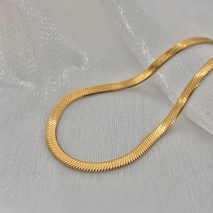 Detailed macro view of golden double-layered flat snake bone chain with metallic texture