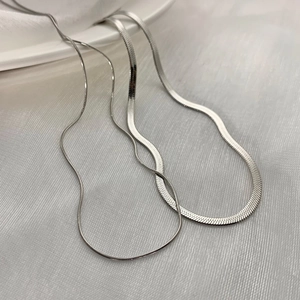 Detailed view of layered silver herringbone and round link chains on white silk