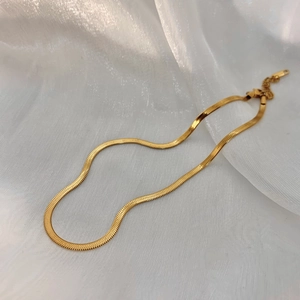 Close-up of gold double-layer flat snake bone necklace on white silk background