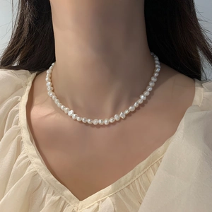 Collier élégant en perles baroques porté par un mannequin sur fond de chemisier crème