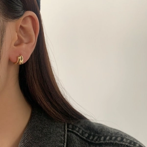 Close-up of a minimalist gold twisted teardrop hoop earring worn by a model