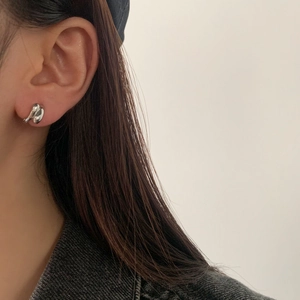 Close-up of liquid metal style twisted silver earrings worn by a model in soft lighting
