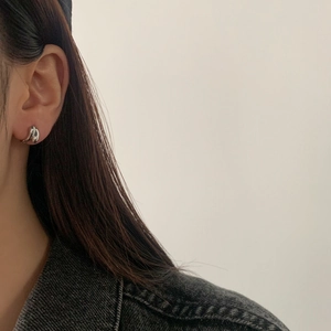 Detail view of silver knotted hoop earrings worn by a model in a modern style