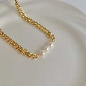 Macro detail of gold chunky link chain necklace featuring three glossy freshwater pearls