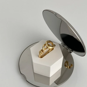 Detail view of a gold-plated knotted geometric open ring on a white display block