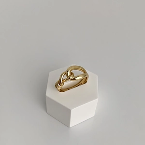 Macro detail of high-polish gold knotted geometric open ring on minimalist white display