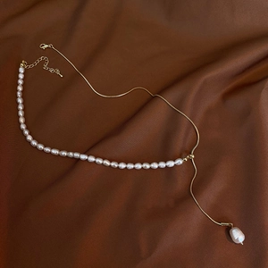 Detailed view of asymmetric freshwater pearl necklace with gold chain on silk fabric