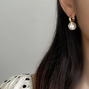 Detail of a large white pearl earring with gold-plated geometric hook on a model
