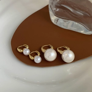 Detail of two pairs of shell pearl earrings with gold plating on a brown leather texture