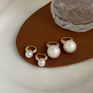 Detail view of double-sided gold-plated pearl hoop earrings on a leather surface