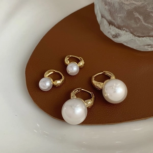 Detailed view of double-sided gold-plated pearl hoop earrings in two sizes on a leather pad